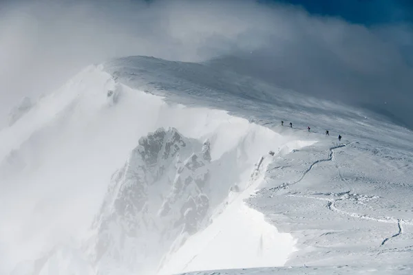 Прекрасный вид на высокие заснеженные горные хребты и лыжников, идущих вдоль него — стоковое фото