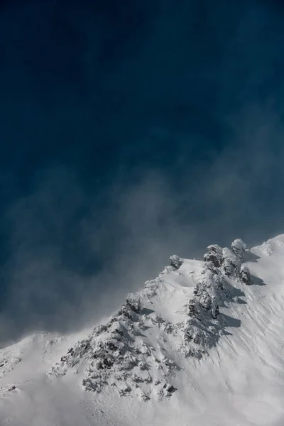 Gusts of wind blow snow off the rocks at the top of the mountain. — Photo