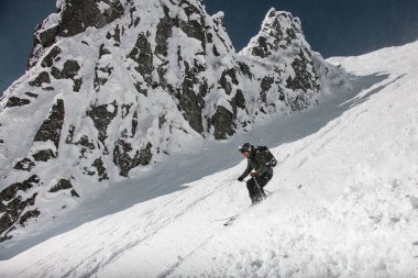 Kahverengi ve siyah spor giyimli kayakçı go-pro kameralı oh kaskı karla kaplı yamaçlardan kayıyor