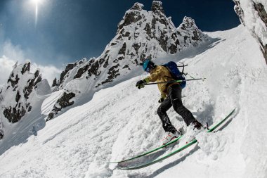 Kayakçı bej ve siyah spor kıyafetleriyle go-pro kameralı oh kaskı karla kaplı yamaçlardan kayıyor
