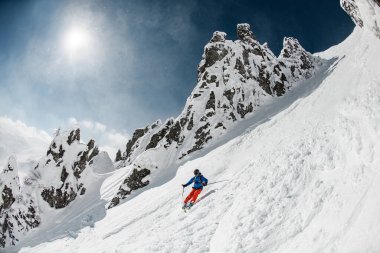 Parlak spor kıyafetleriyle kayak yapan kayakçı hızla kayak pistlerinde kayıyor..