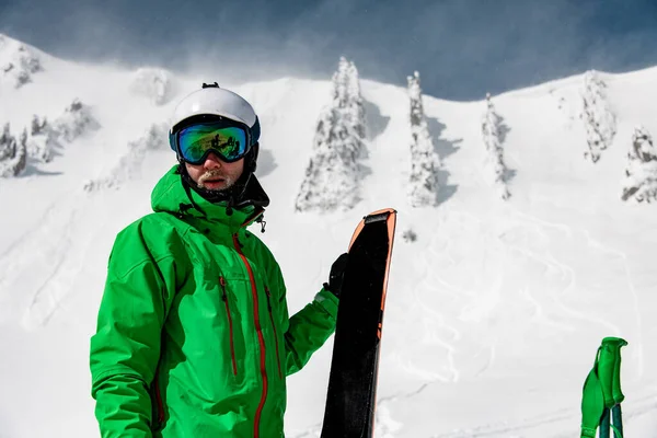 Передня фотографія чоловічого лижника в яскравій лижній куртці та окулярах, що тримають пару лиж . — стокове фото