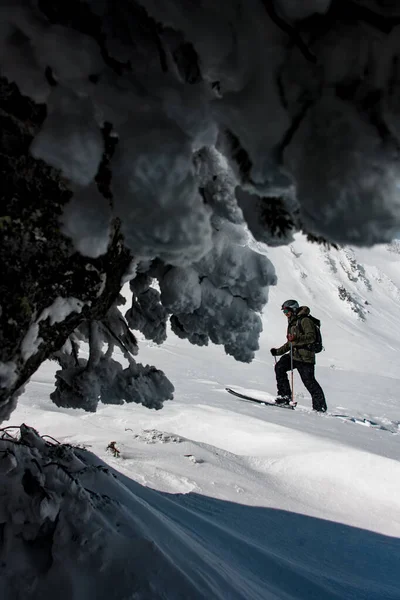 身穿滑雪服、头戴背包头戴头盔的男子滑雪者手持滑雪杆在雪地中穿行的侧面照片. — 图库照片
