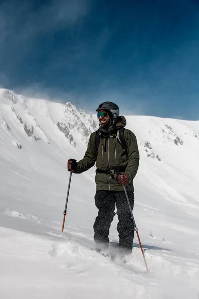 Genç, yakışıklı, gülümseyen kayakçı elinde kayak sopalarıyla yan tarafa bakıyor. — Stok fotoğraf