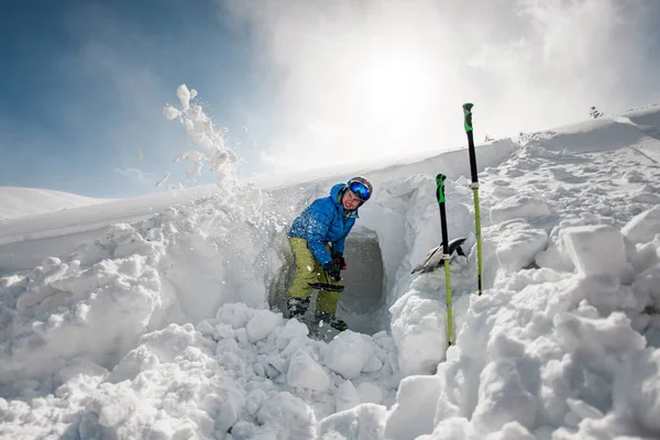 Yound man in bright ski suit with shovel carefully digging the snow — стоковое фото