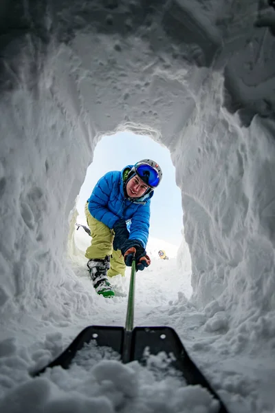 Молодой человек в ярком лыжном костюме с сапогами осторожно рыл тоннель в снегу. — стоковое фото