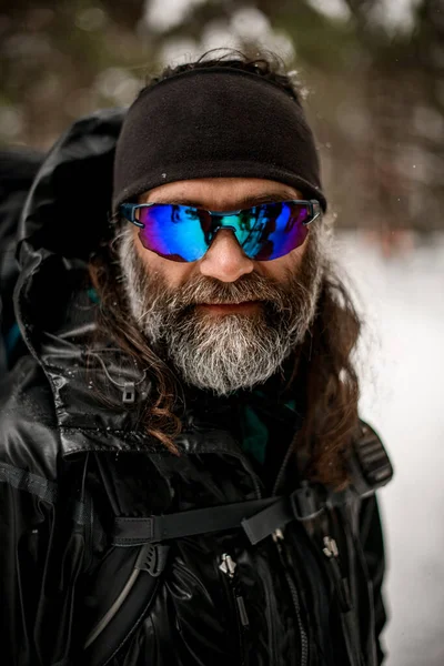 Ski pria dengan jenggot mengenakan jaket hitam dan ikat kepala bulu domba dan kacamata terhadap latar belakang kabur — Stok Foto