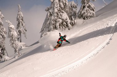 Genç snowboardcu, parlak rengarenk giyinmiş, her tarafı karla kaplı.