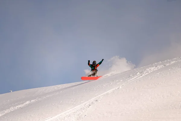 उज्ज्वल ओवरऑल में सक्रिय स्नोबोर्डर पाउडर बर्फ पर स्प्लिटबोर्ड पर पहाड़ के नीचे स्लाइड करता है — स्टॉक फ़ोटो, इमेज