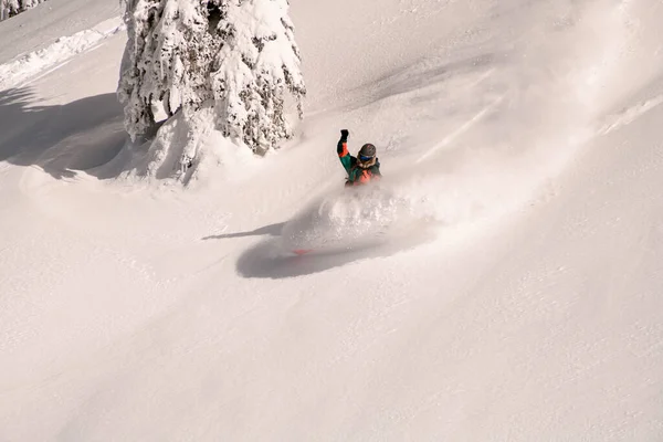 Aktywny snowboardzista w jaskrawym wielobarwnej ogólnej jazdy w dół na desce rozpryskujący śnieg — Zdjęcie stockowe