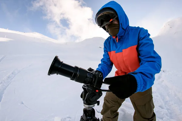 Fotografer pria berdiri di gunung bersalju di siang hari dan mengambil gambar dengan kamera digital Stok Lukisan  