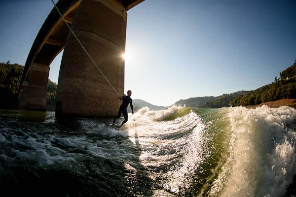 Nagyszerű kilátás a srác búvárruha tartó kötél fogantyú és lovaglás Wakesurf fórumon hullám. — Stock Fotó