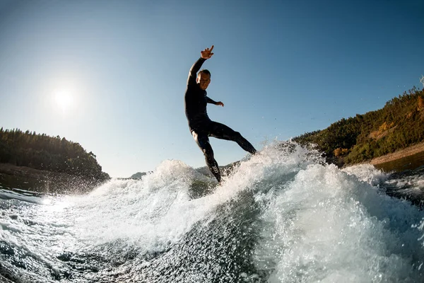 Active sports man in wetsuit balancing on splashing wave on a wakesurf — Stockfoto