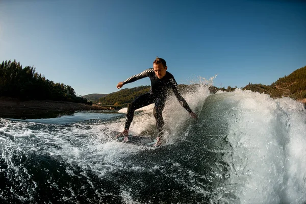 Sportlicher Mann im Neoprenanzug auf Waksurfbrett reitet die plätschernde Welle hinunter — Stockfoto