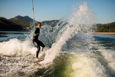 Aktif insan binicisi ipin sapını tutar ve güçlü bir şekilde su sıçratma tahtasının üzerinde süzülür..