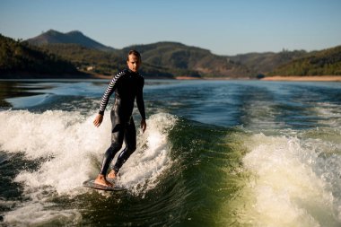 Dalgıç kıyafetli çekici bir adam ustalıkla su sıçratan dalgalara biniyor.