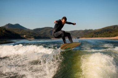Dalgıç kıyafetli adam dublörlük yapar ve nehrin üzerinde bir dalganın üzerinde zıplar