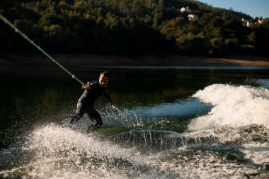 Atletik adam ipin sapını tutuyor ve güçlü bir şekilde su sıçratma tahtasına biniyor..