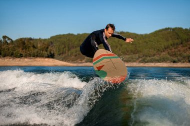 Atletik bir adam nehir dalgasının üzerinden atlıyor.