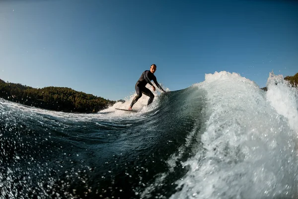 Athletic man in wetsuit on wakesurf riding down the splashing wave —  Fotos de Stock