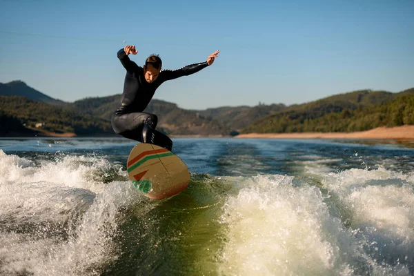 Sportlicher Mann im Neoprenanzug macht Stunt und springt auf einem Wakesurf über die Flusswelle — Stockfoto