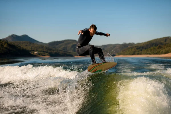 Dalgıç kıyafetli adam dublörlük yapar ve nehrin üzerinde bir dalganın üzerinde zıplar