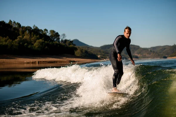 Attractive man in wetsuit on wakesurf riding on splashing river wave — Stockfoto
