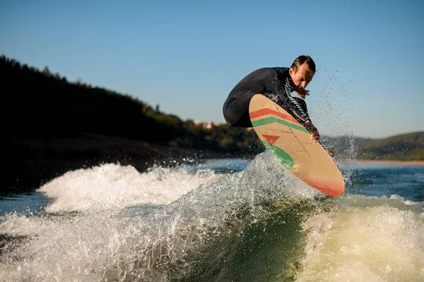 Dalgıç kıyafetli uyanık nehir dalgalarının üzerinde bir sörf tahtasına atlıyor.