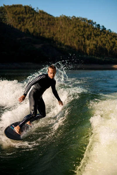 Athletic man on wakesurf riding down the splashing wave — Stockfoto
