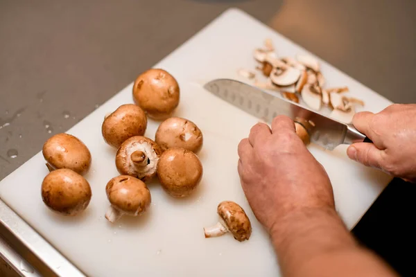 Man cutting champignon into slices with knife on cutting board — Stockfoto