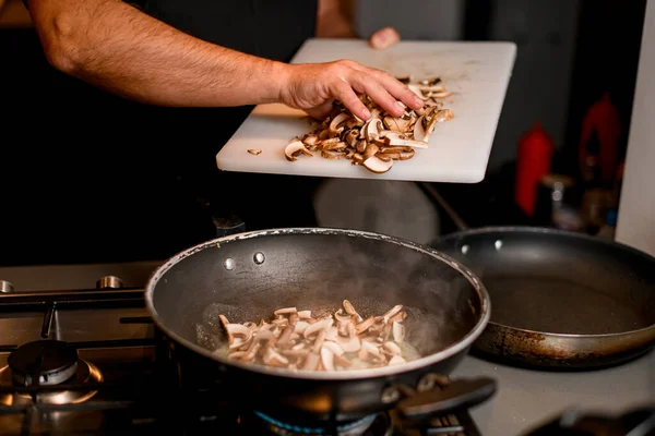 Male chef pours chopped champignons from cutting boards into a frying pan — Stock Photo, Image