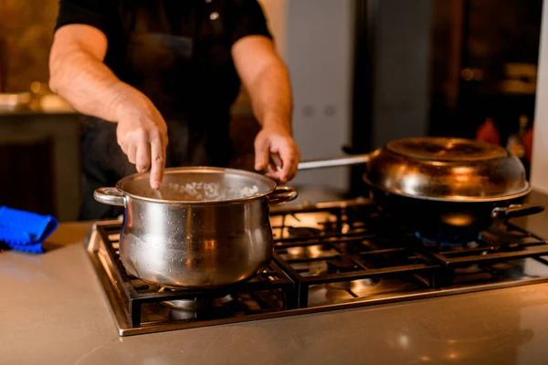 Pan on the stove and male chef with a spoon stir the dish in it — Stock Photo, Image