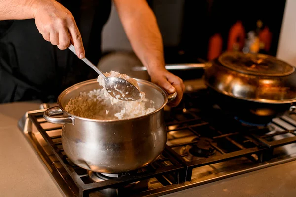 Zbliżenie męskiej dłoni wyjmuje gotowany ryż z patelni łyżeczką — Zdjęcie stockowe