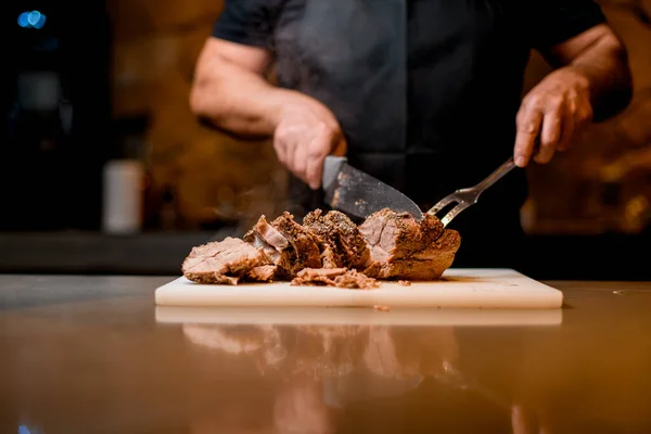 Selective focus on delicious fried meat which man cuts to slices on cutting board. — Stockfoto