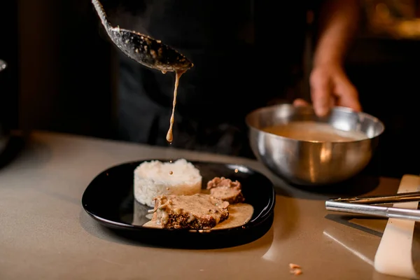 Samiec gotować dokładny sos wylewania na plasterek smażonego mięsa na talerzu — Zdjęcie stockowe