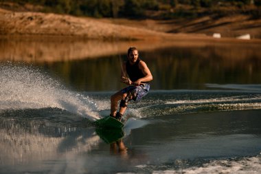 Atletik sakallı adam halat tutuyor ve nehirde hızla wakeboard sürüyor..