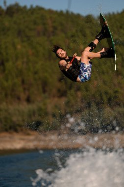 Close-up of energy male wakeboarder jumping and flips on wakeboard