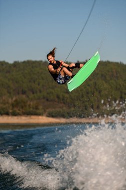 Enerji atletik bir adam elinde ip tutuyor ve parlak bir wakeboard ile havaya zıplıyor.