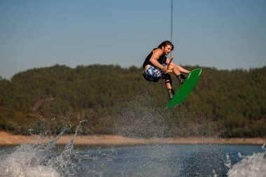Çekici sakallı adamın elinde ip varken Wakeboard 'da nehrin üzerinden atlaması inanılmaz bir manzara.
