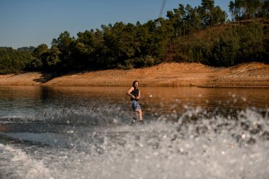 Yakışıklı adam halatı tutuyor ve sörf tahtasında nehir dalgalarında yüzüyor.