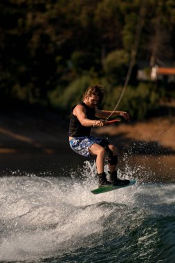 Atletik adam halatı tutuyor ve dalgaya atlıyor..