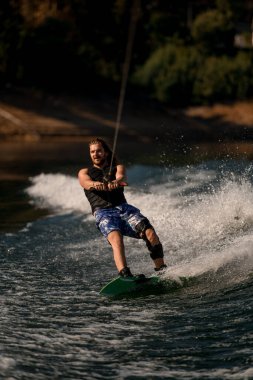 Atletik adam halatı tutuyor ve dalgada süzülüyor..