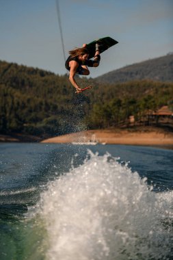Wakeboardcu tehlikeli dublörlük yapıyor atlıyor ve su sıçratan nehir dalgaları üzerinde sallanıyor.