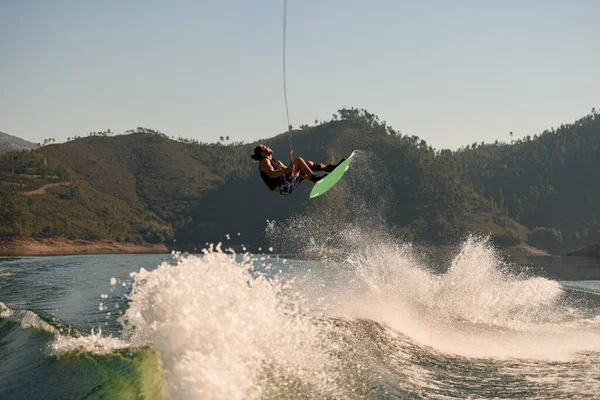 Aktif sporcu Wakeboard 'la mavi gökyüzüne ve yeşil tepelere doğru atlıyor.