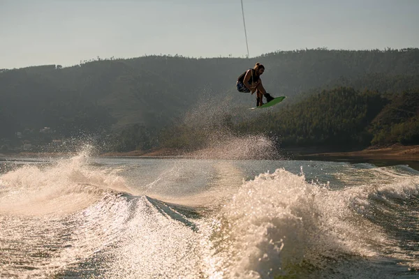Amazing view of the splashing wave and active man jumping in the air with wakeboard — Zdjęcie stockowe