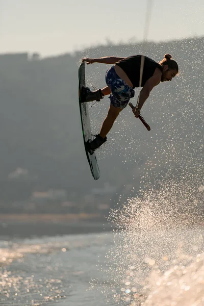 Primer plano del hombre sosteniendo una cuerda y saltando en el aire con wakeboard —  Fotos de Stock