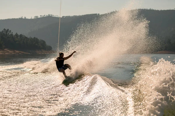 Active man holds rope and energetically balancing on splashing wave on wakeboard — Stock Photo, Image