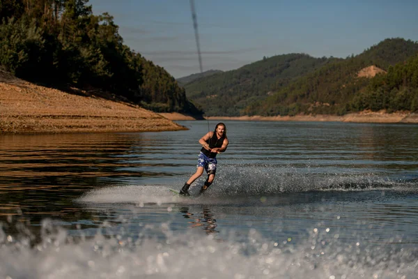 Great view on attractive bearded man holding rope and riding on the river wave on wakeboard — Zdjęcie stockowe