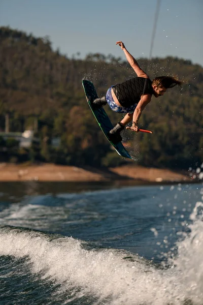 Back view of active man with wakeboard jumping over splashing wave. — Stockfoto