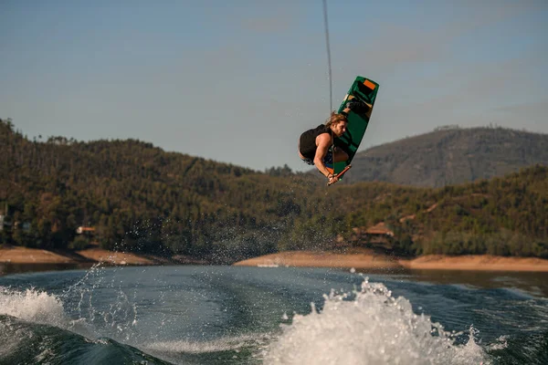 View of man with wakeboard masterfully jumping high over splashing wave. — Zdjęcie stockowe